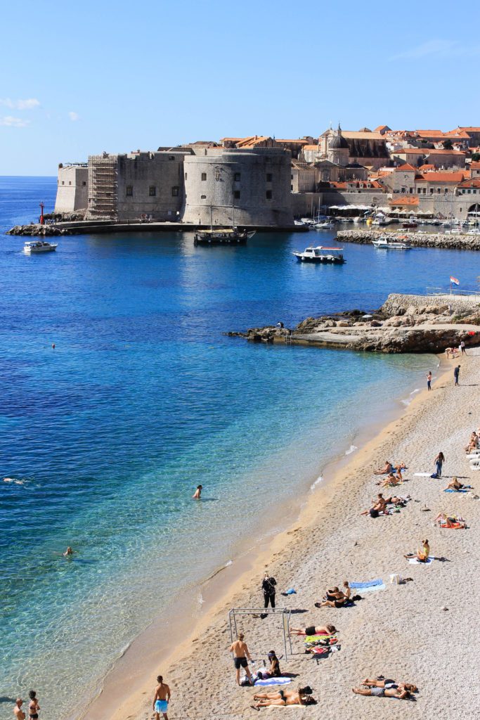 Banje Beach with the walls of Dubrovnik and harbor in the background. Banje beach is one of the best things to do in Dubrovnik 