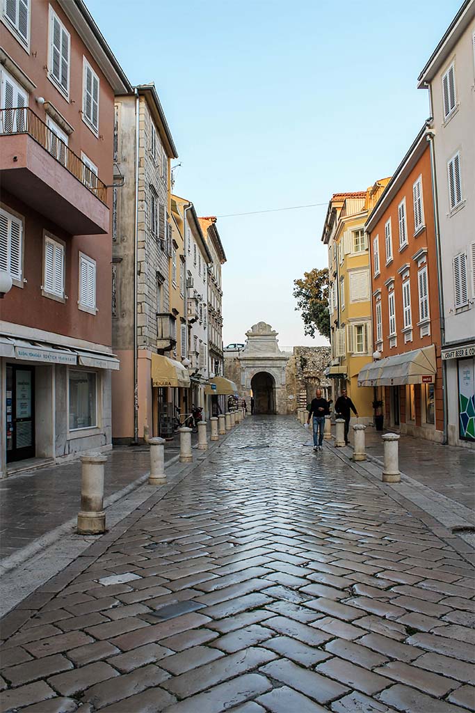 Shiny marble streets and old buildings looking towards Zadar's walls and gate in Croatia