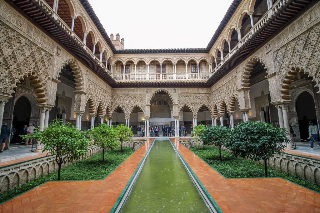 Pool inside the Real Alcazar with raindrops and scrolled arches around it. This is one of Seville's most iconic images and is beautiful to see in person. The Moorish style architecture is beautiful and well worth visiting. 