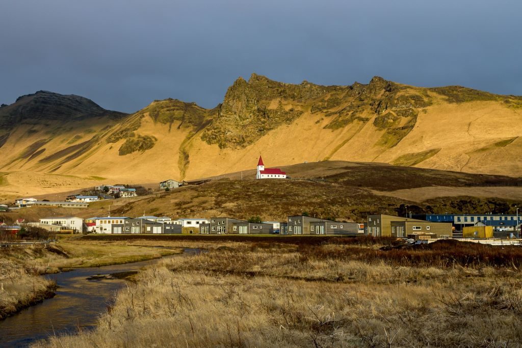 The town of Vik with mountains behind it and a red roofed church that sits above the town.