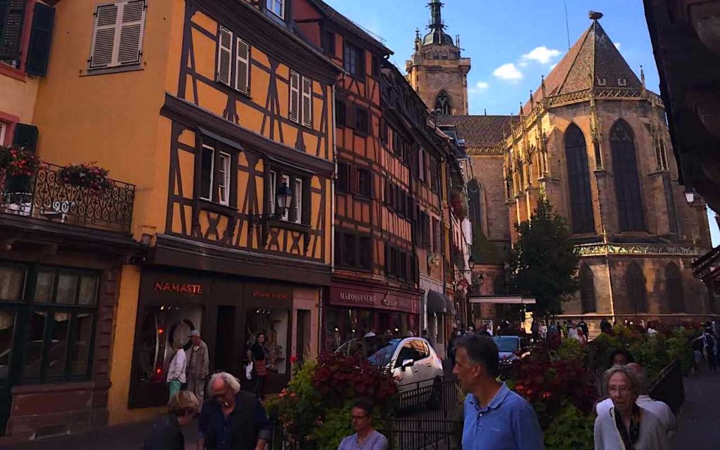 The half timbered buildings that are characteristic of Colmar with a church in the background. Colmar is a must see city in France that has delicious Alsatian food and a beautiful Little Venice area