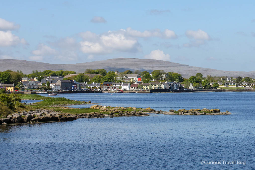 View of a village in County Galway with the Burren behind it and the bay in front. The Burren is often visited along with the Cliffs of Moher on a day trip from Galway.