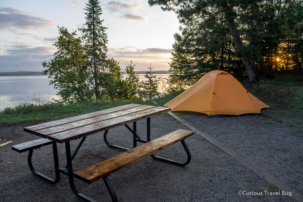 Camping at Sleeping Giant Provincial Park in Thunder Bay, Ontario, Canada at sunrise with a picnic table and orange tent above Marie Louise Lake.