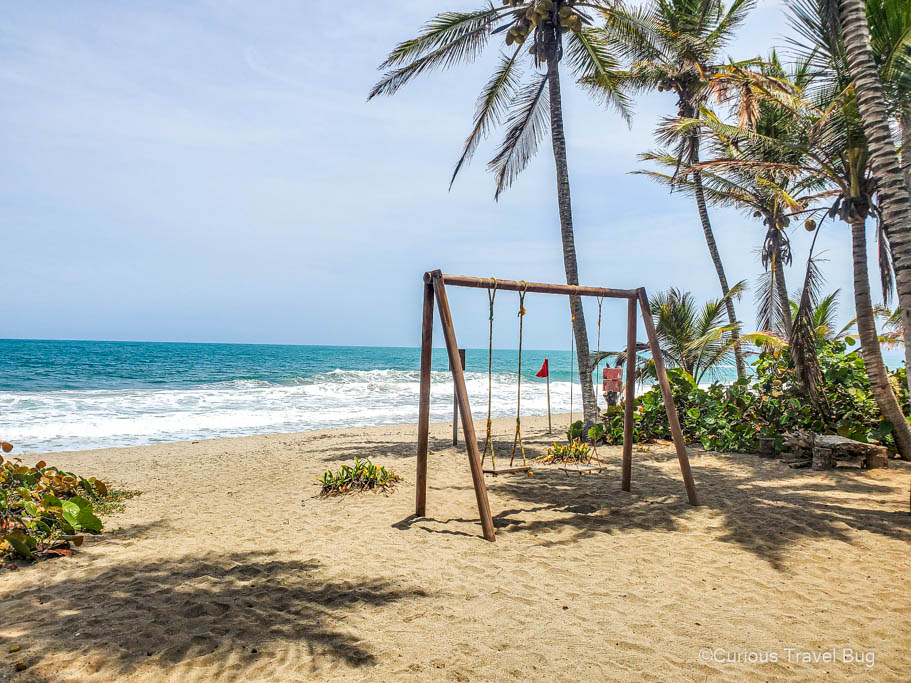 Swing in front of a sand beach with palm trees and the clear waters of the Colombian Caribbean coast. The Caribbean Sea near Tayrona National Park is a must see location in Colombia