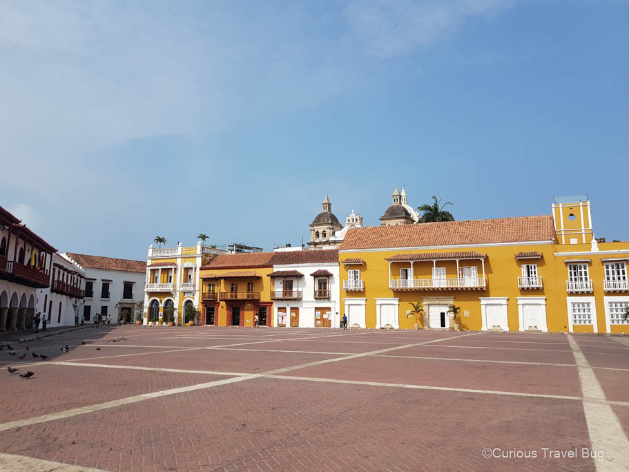 Plaza de la Aduana in Cartagena, Colombia with colonial style buildings painted a bright yellow. Exploring Cartagena's old town is one of the best things to do in Colombia