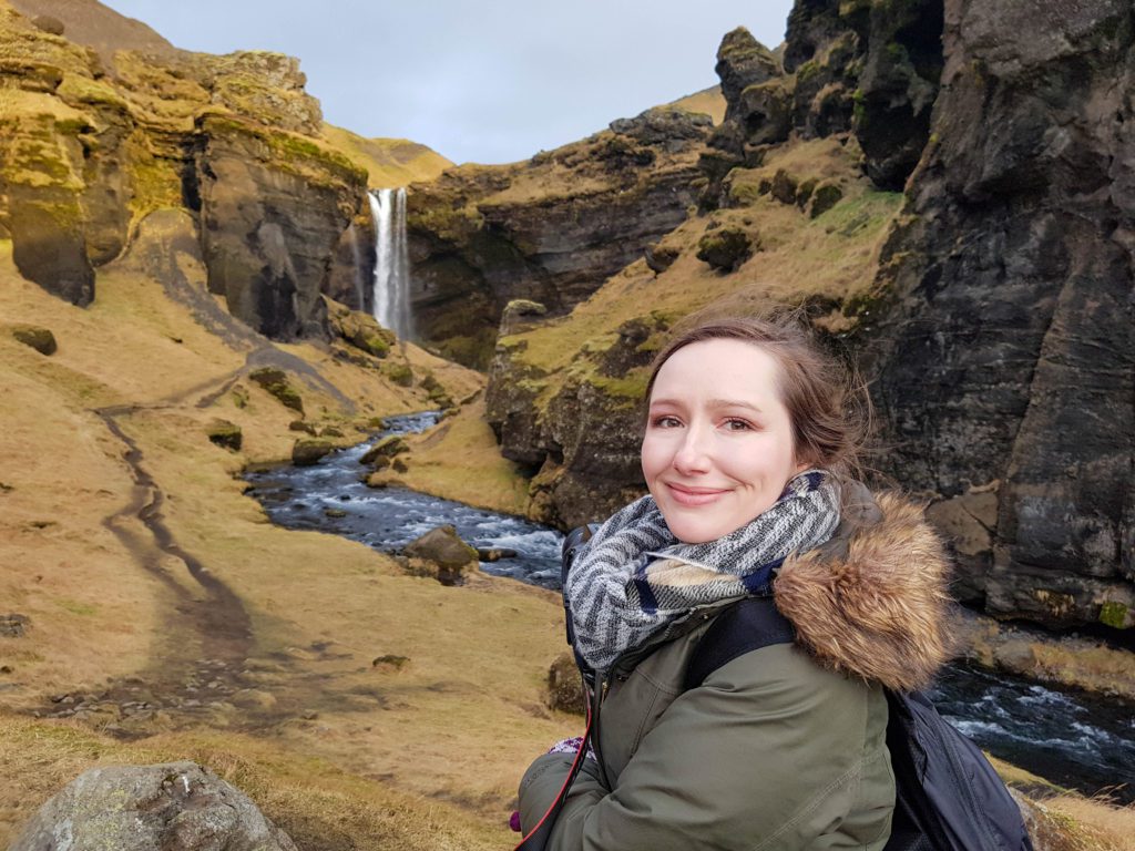 Woman faces the camera with a waterfall and river behind her in Iceland