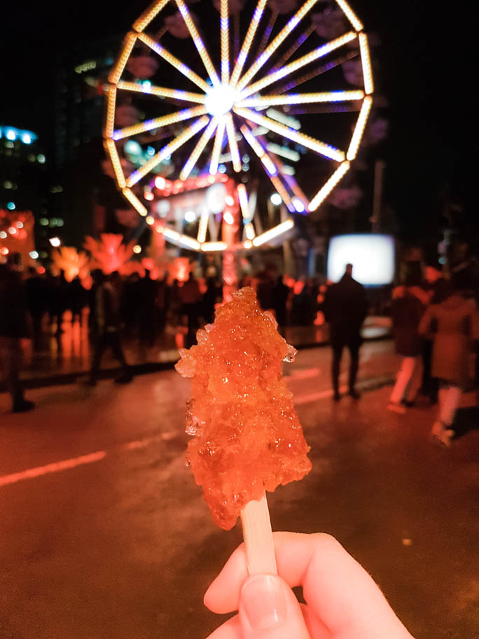 A traditional maple taffy stick in Montreal at night with a ferris wheel lit up in the background