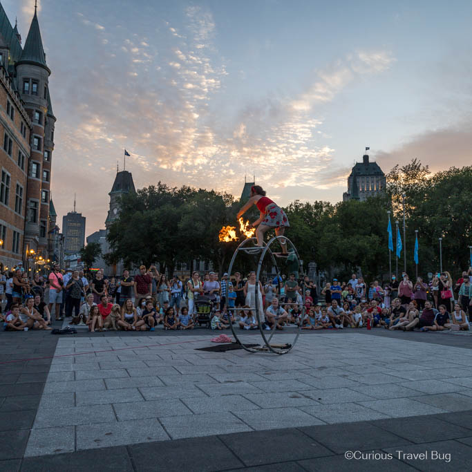 A performer balances on a wheel while swinging fire balls in front of the Chateau Frontenac