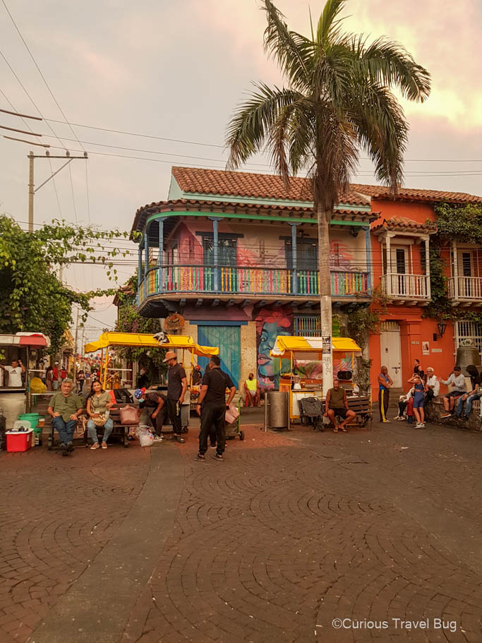The Plaza de la Trinidad in Getsemani, Cartagena with a tall palm tree and street vendors selling food.