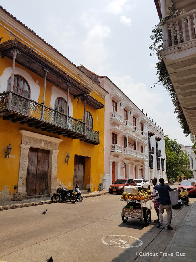Street of Cartagena with colonial style buildings and street vendors selling coconuts and fruit.