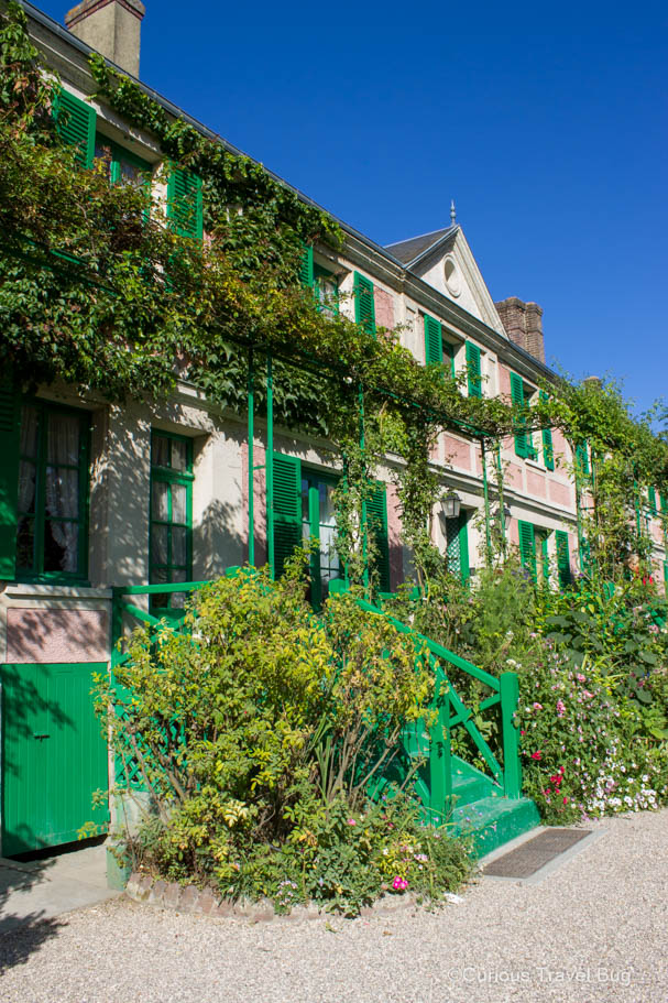 Claude Monet's Giverny House with pink brick and green shutters with vines growing all over it.
