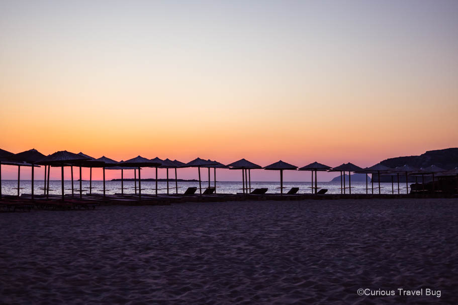 Sunset over Falasarna Beach with parasols in shadow. Falasarna is the perfect place to base yourself in Western Crete to explore the nearby beaches and relax in the sun.