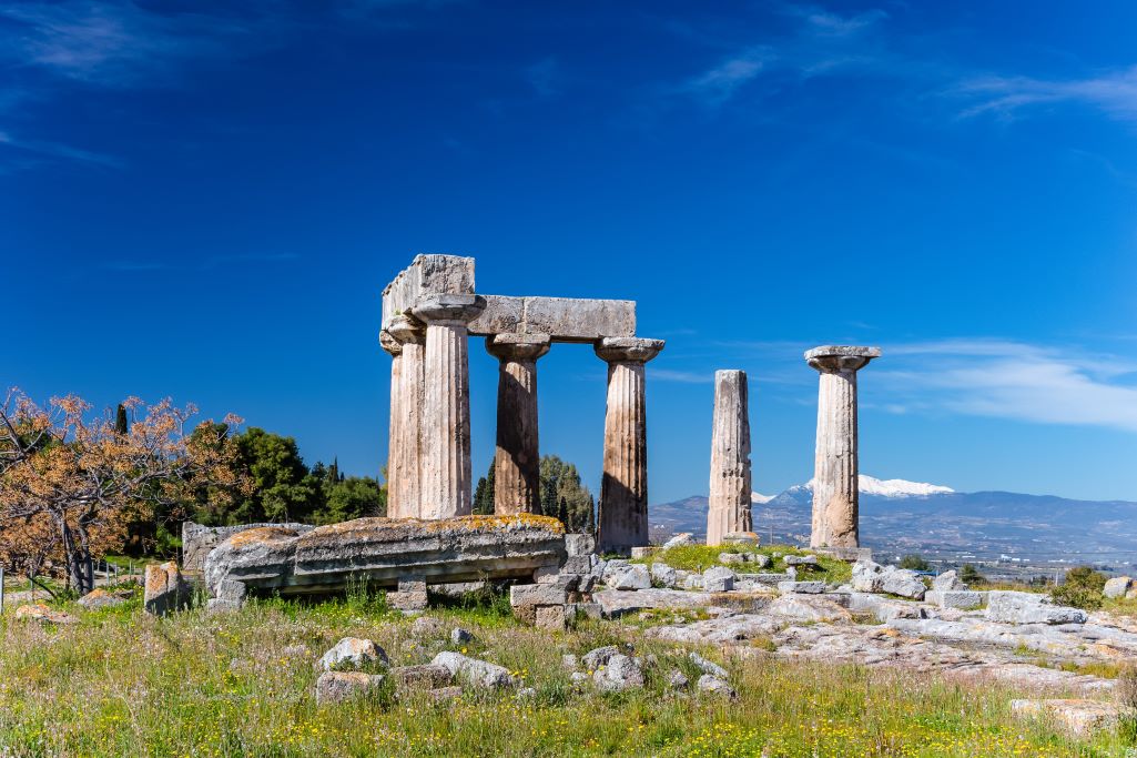 Doric column ruins at the Corinth Ruins in Greece with white capped mountains in the background, you can visit Corinth on one of the best day tours from Athens in only half a day.