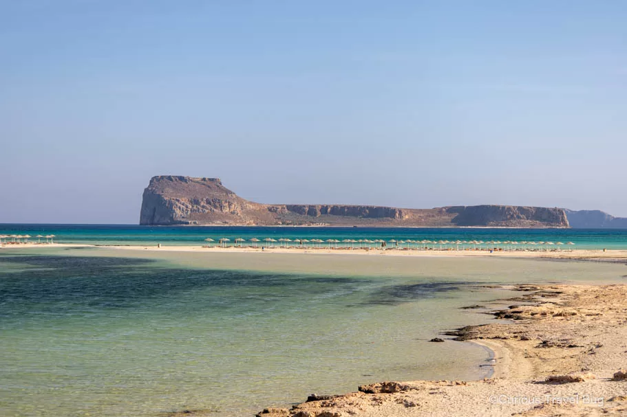 View of Balos Lagoon with loungers and umbrellas with Gramvousa Island in the background