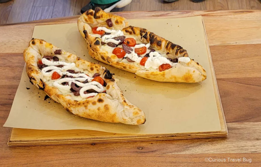 Boat shaped pizza with black olives, tomatoes, and white sauce served in Athens on a street food tour