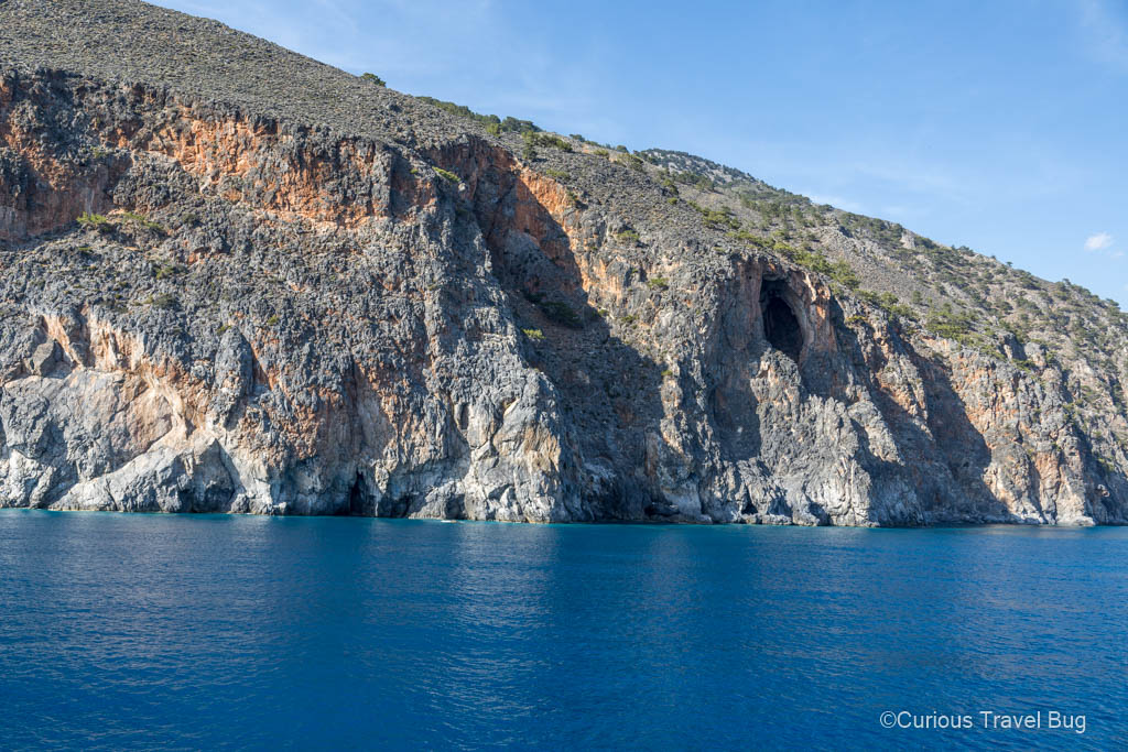 Blue Libyan Sea with cliffs rising out of it and a large cave is present when viewed from the ferry between Agia Roumeli and Sougia on the coast of Crete