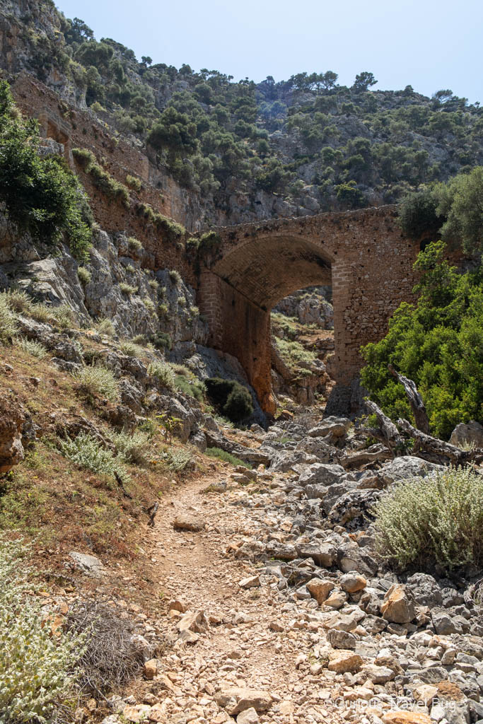 View of the Katholiko Monastery bridge with path below and mountains behind it, in the Akrotiri Peninsula of Crete